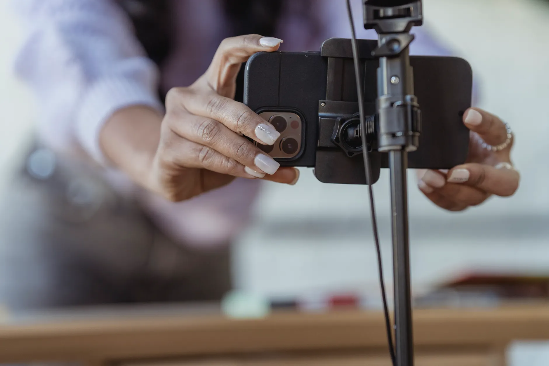 Crop unrecognizable female setting mobile phone on tripod while recording vlog on blurred background